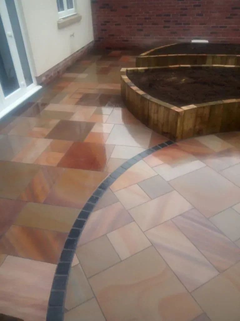 The circular sandstone patio at the centre of the garden, ringed with dark setts and edged by a timber sleeper bed
