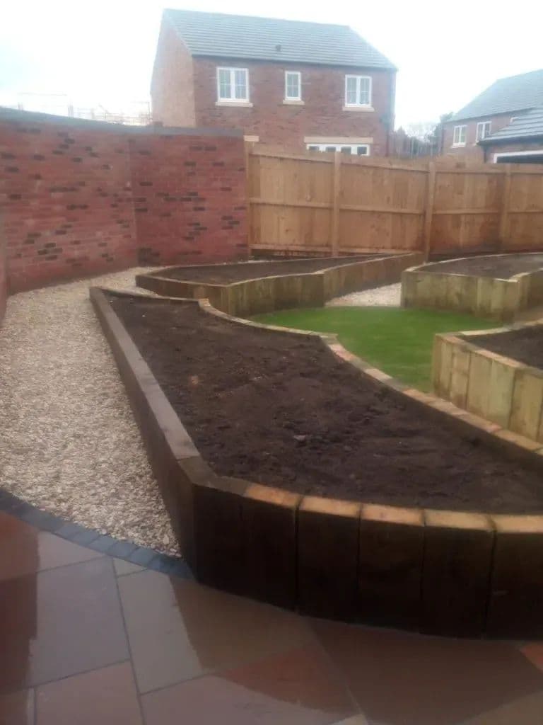 Curved timber sleeper beds running along the fence, with gravel, a strip of lawn and the sandstone patio beyond