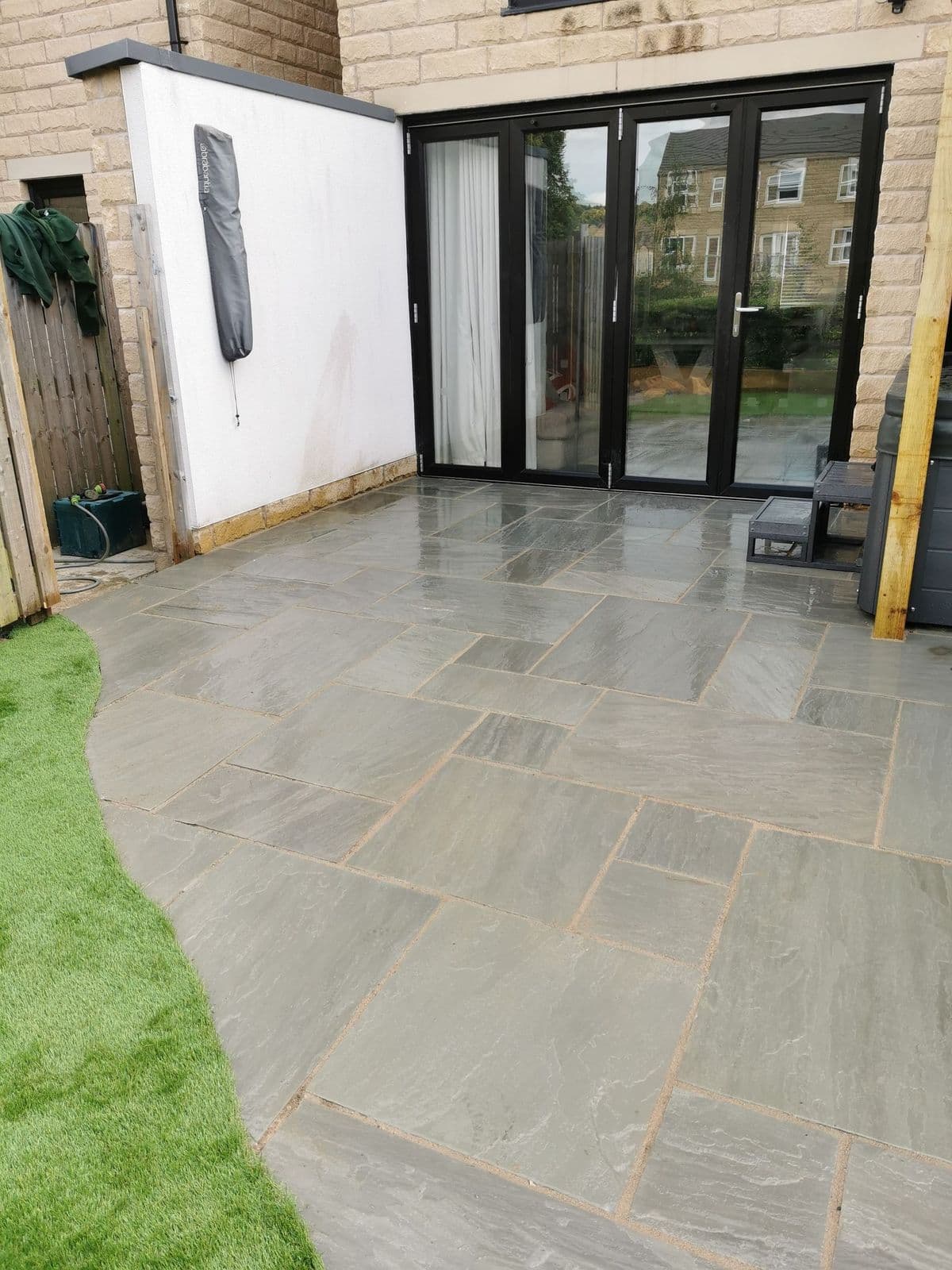 Kandla grey paving with a cut curved front edge running up to the artificial lawn and the bi-fold doors