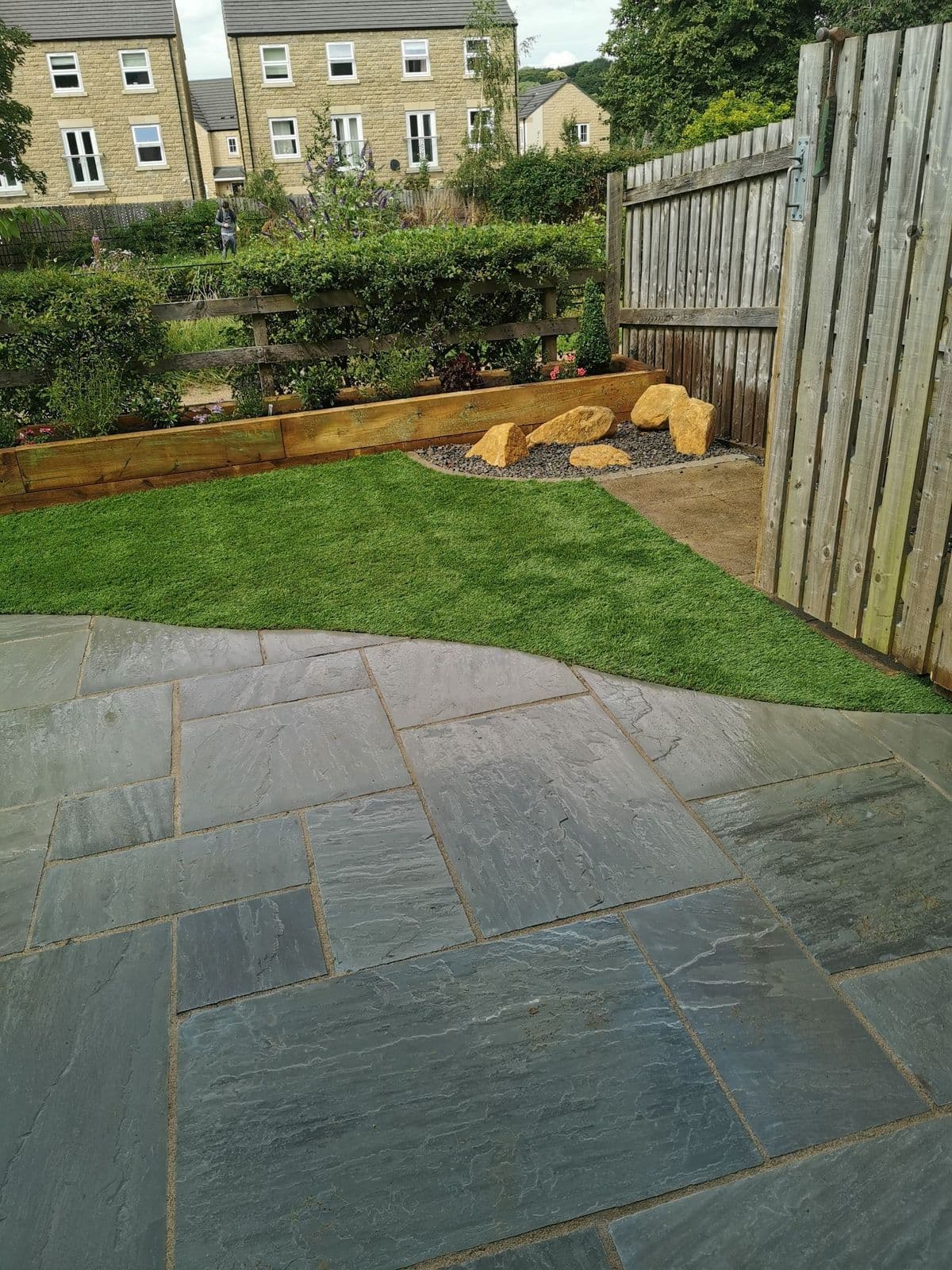 The finished garden: Kandla grey patio, artificial lawn and a raised sleeper planter with cobbles and rocks