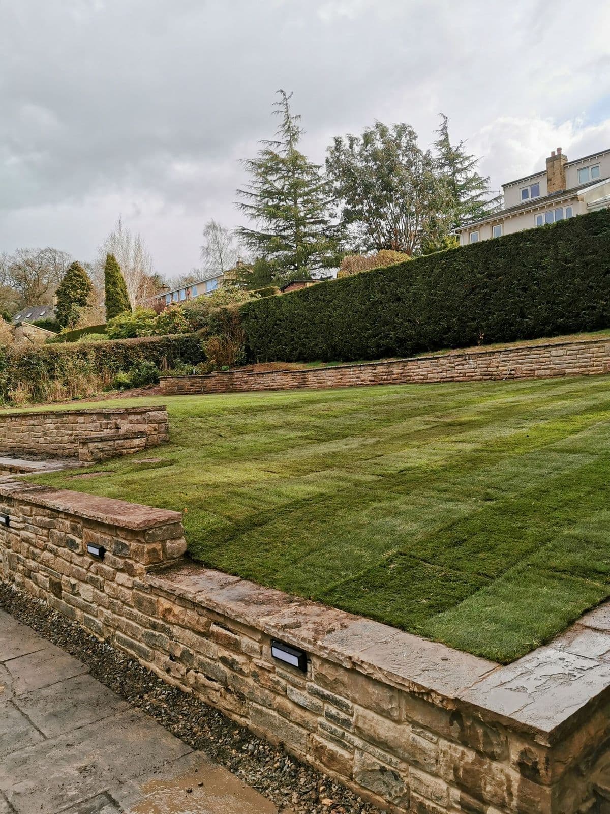 A random stone retaining wall with lights set into it, holding back the newly turfed lawn