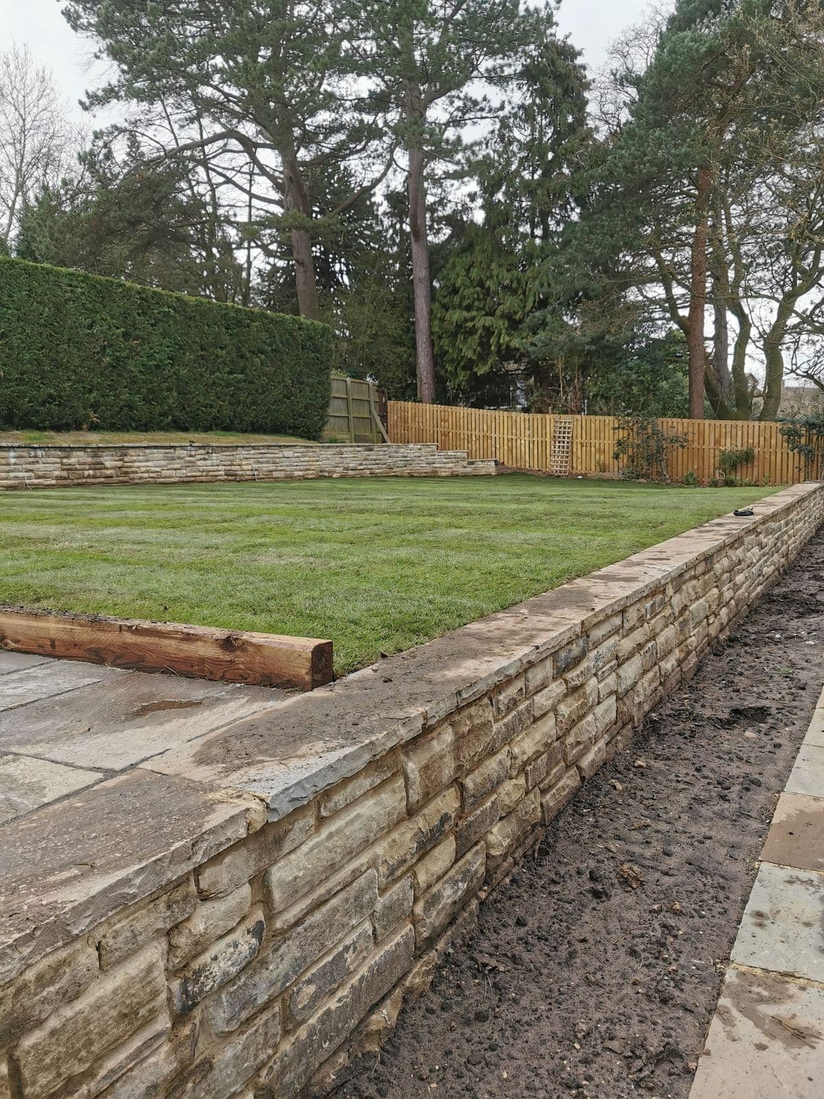 The stone retaining wall running the length of the new lawn, with paving along the foot of it