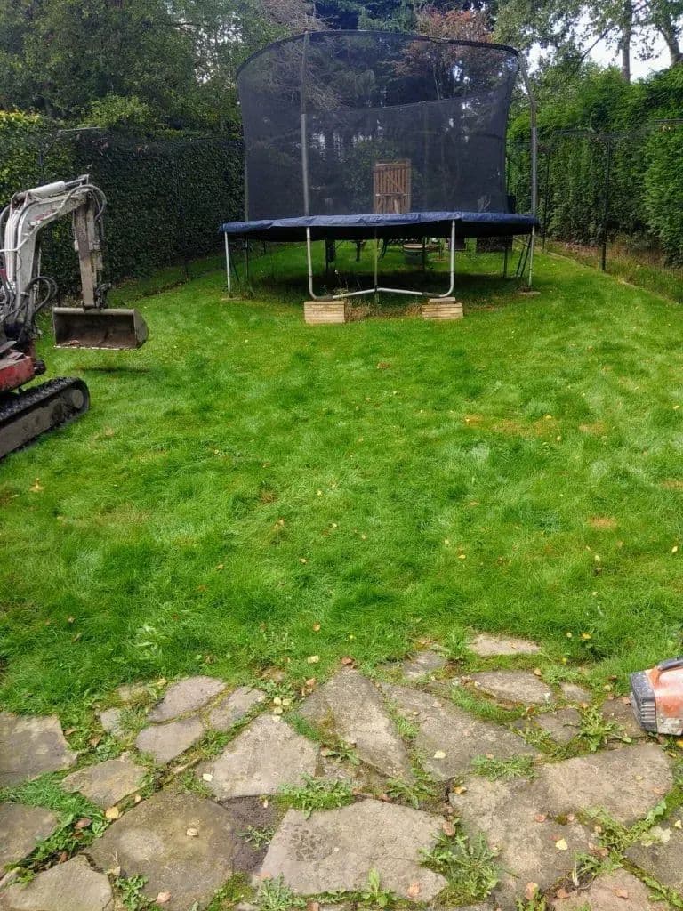The digger at work on the sloping lawn beside the trampoline