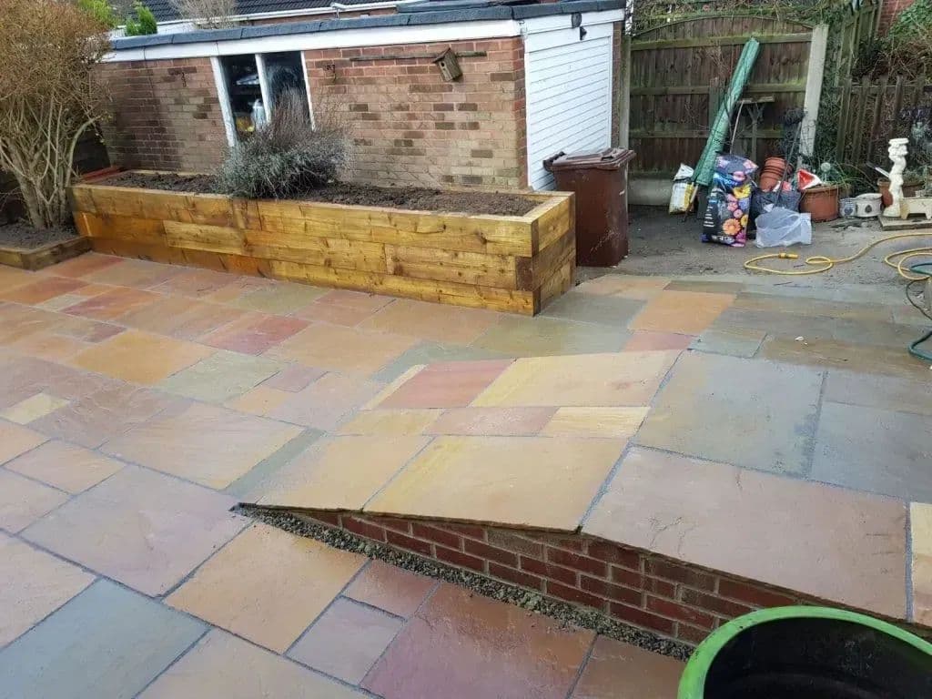 The paved garden with a long timber sleeper planter along the boundary and a ramp cut into the paving
