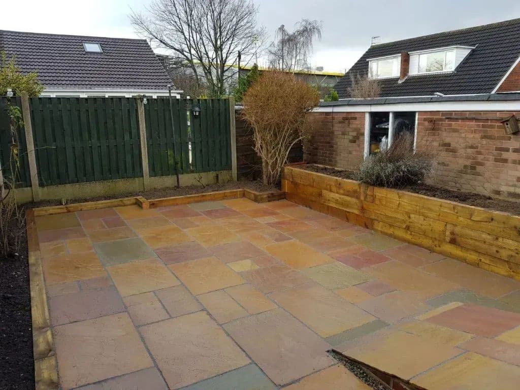 Sandstone paving laid right across the garden, with a sleeper planter under the fence