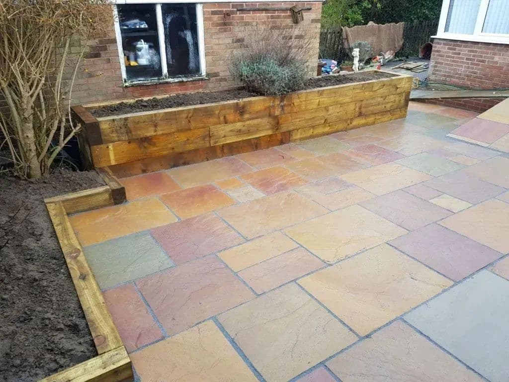 A timber sleeper planter set above the paving, with a low step down onto the flags