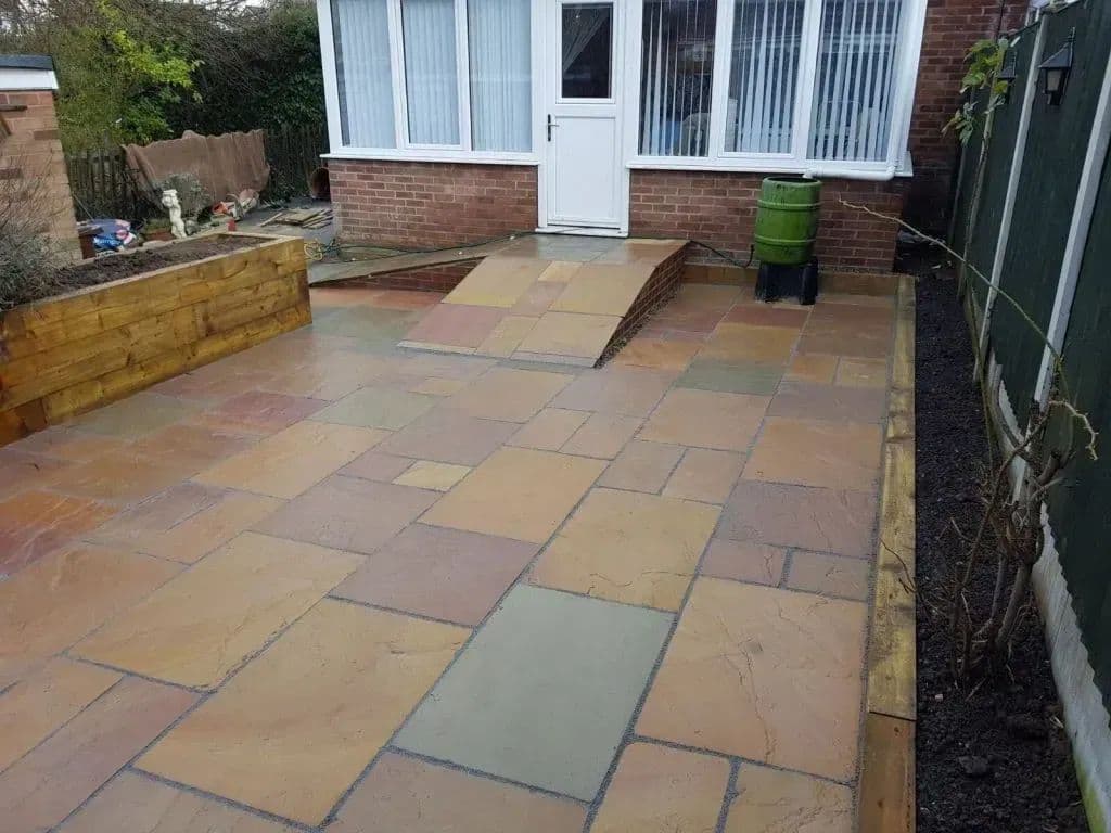 A paved ramp running up to the back door, with the sleeper planter alongside it