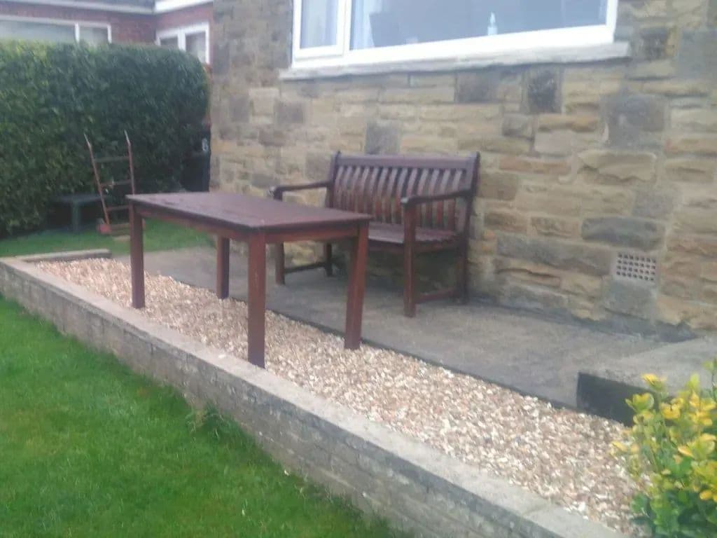 The gravel path along the house wall, with a bench and table on it and stone edging to the lawn