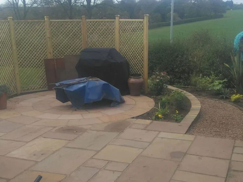 The upper paved area with a trellis screen behind it and the path curving round the lawn to it
