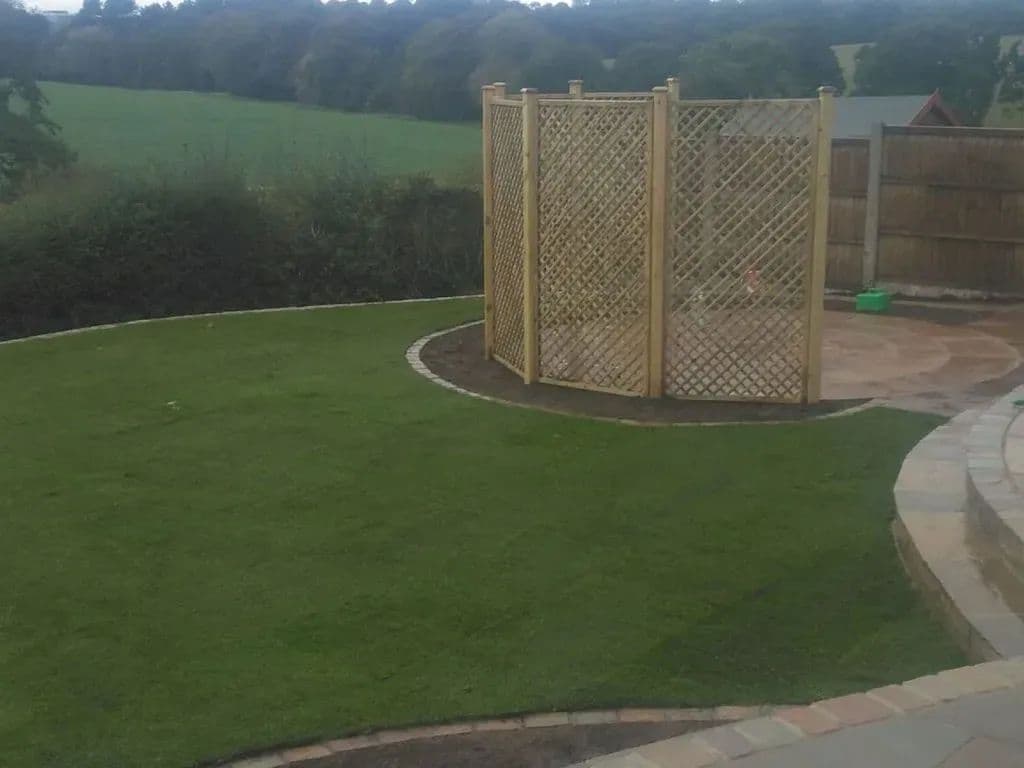 A trellis screen at the top of the garden with the paved path curving past it round the lawn