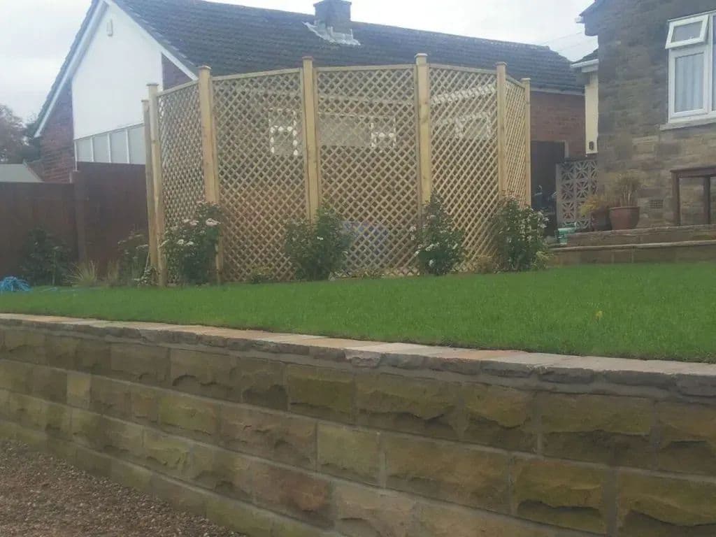 The trellis screen seen from the lawn, with planting along the foot of the walling