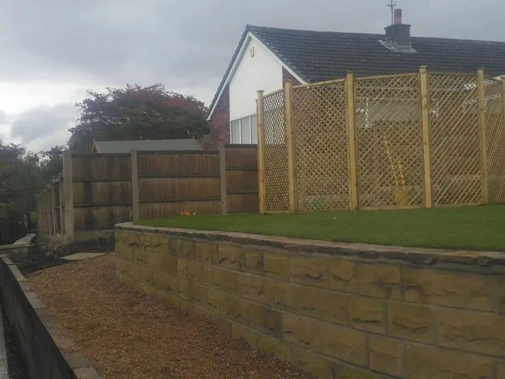 Stone walling along the raised edge of the lawn with the trellis screen behind it
