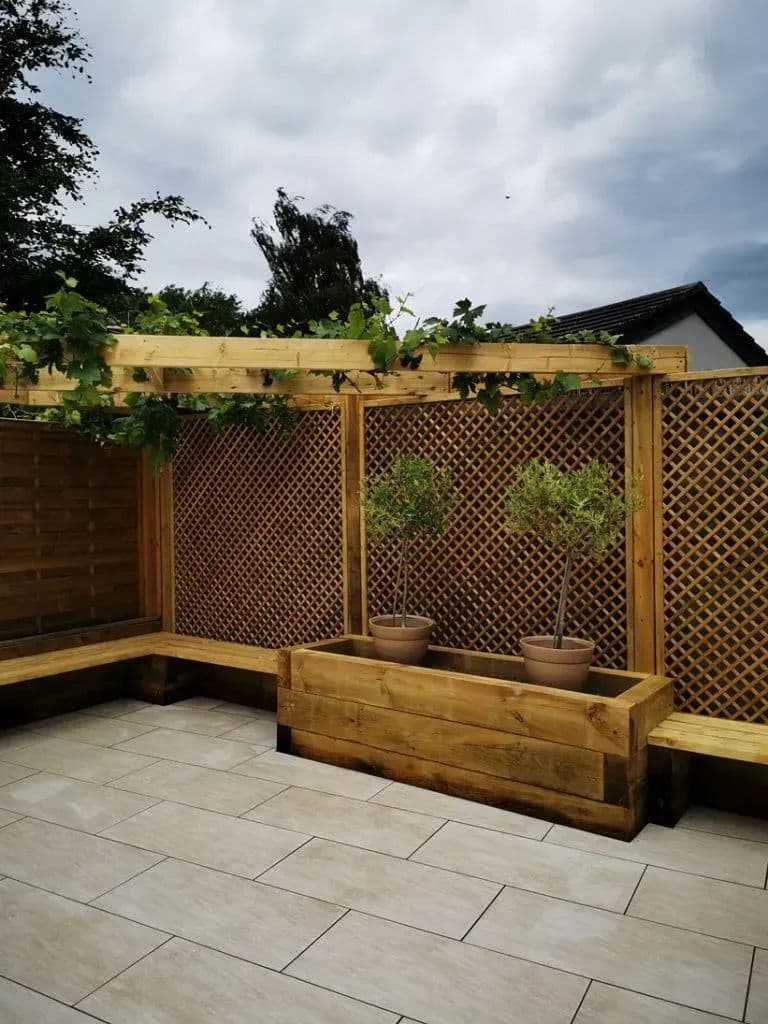 The finished patio from the corner: porcelain tiles, timber seating, planters and the vine overhead