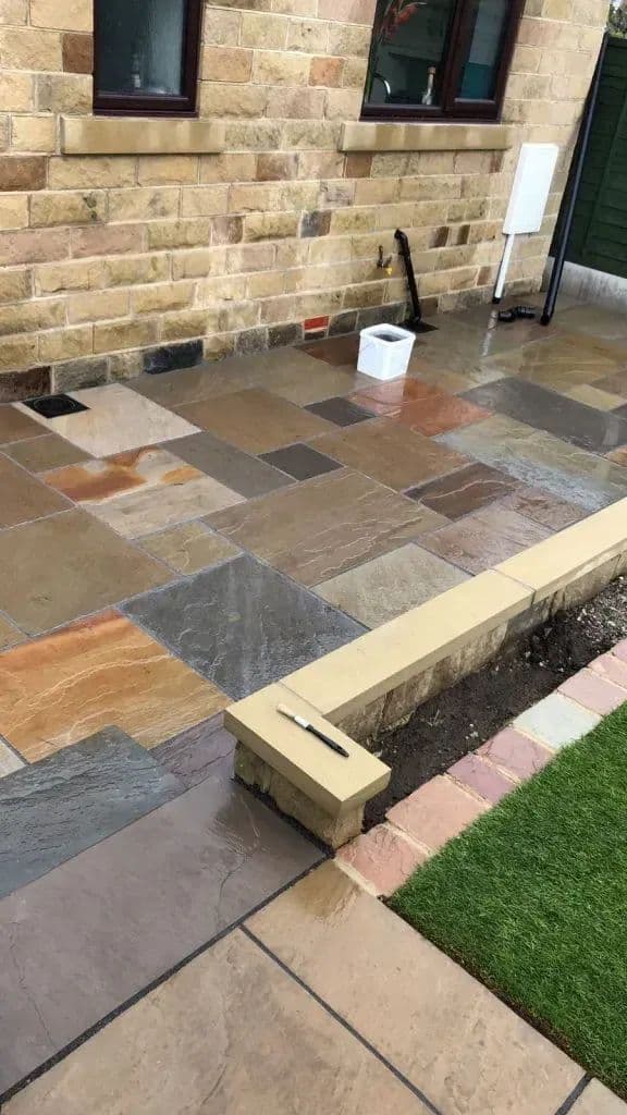 The paving meeting the coping stone of the retaining wall, with the new turf beyond