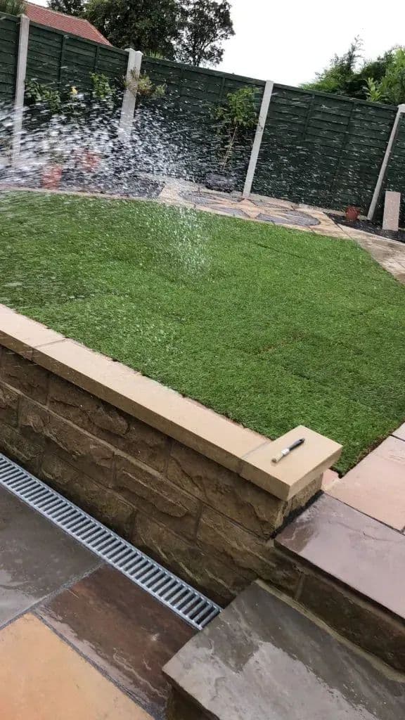 The retaining wall with a drainage channel set into the paving below the new lawn