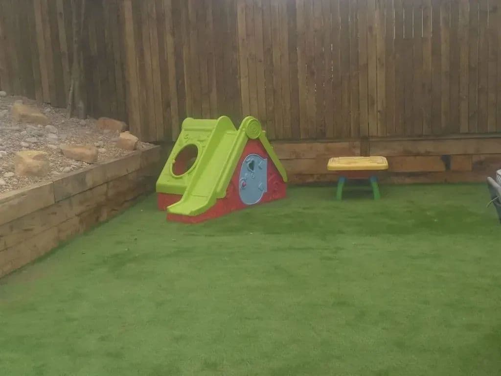 The artificial lawn at the bottom of the garden, enclosed by the sleeper wall and the fence
