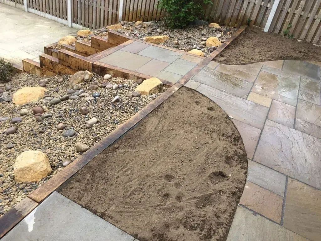 Sandstone paving being set out on the sand bed, with the rockery and sleeper edging behind