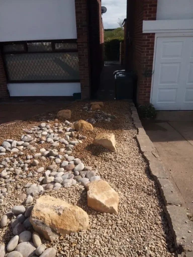 A cobble and boulder bed laid alongside the path at the side of the house