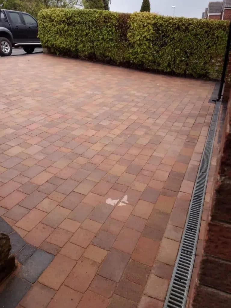 The block paving at the side of the house with a drainage channel set across it