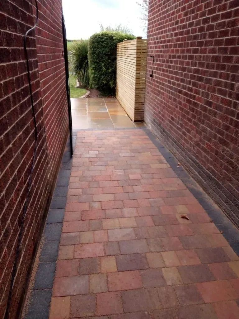 The block-paved passage running between the house wall and the boundary
