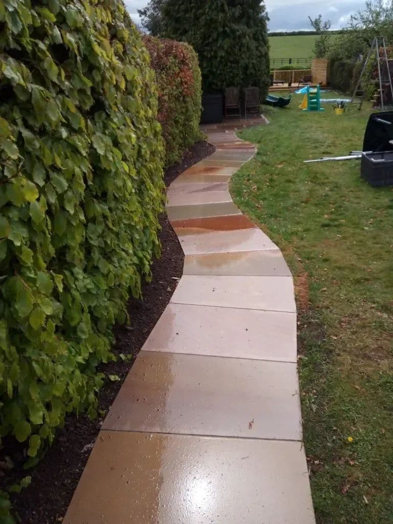 The sandstone path curving along the hedge towards the back of the garden
