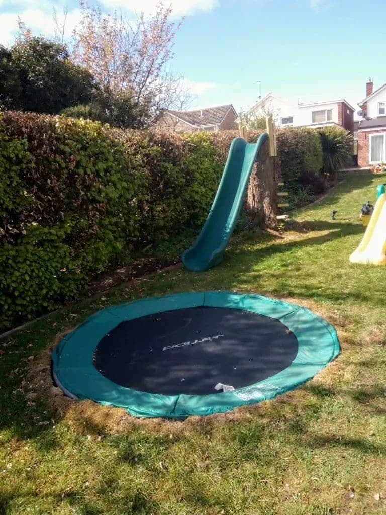 The sunken trampoline set flush into the lawn, with the slide on the bank behind it