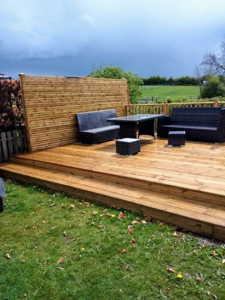 The timber deck built out over the lawn, with seating and a screen behind it