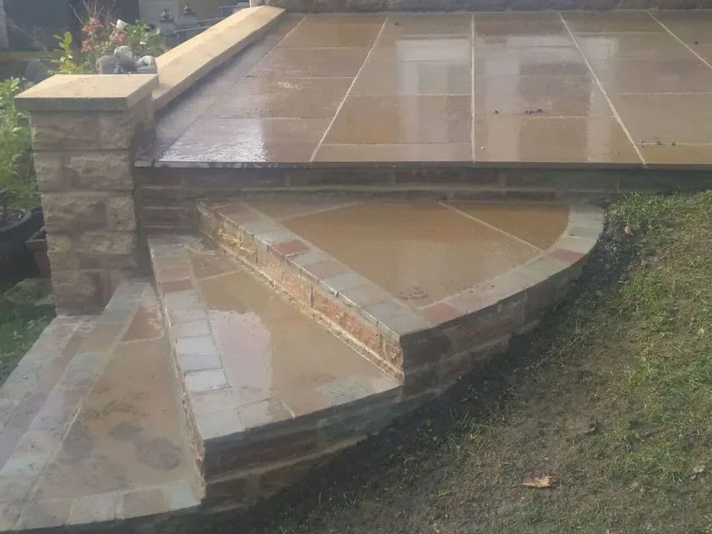 The curved stone steps down from the patio, with the Cottage stone planter and its cobble top alongside
