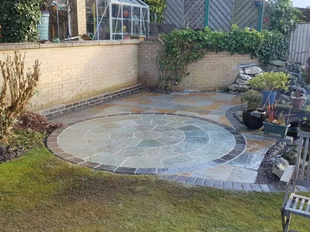 The new patio from the lawn: a three-ring stone circle in old York paving, edged with midnight blue setts