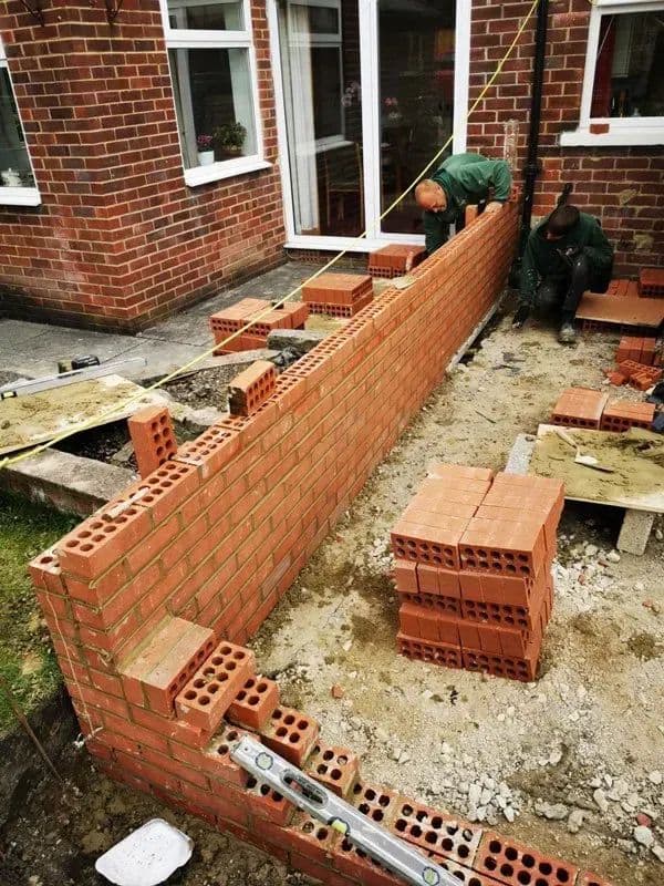 Bricklaying along the line of the new wall, with the level set out above it