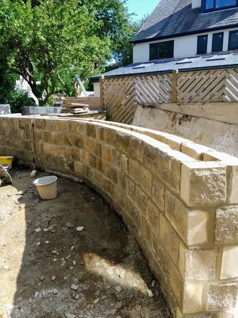 The curved stone wall built into the bank at the top of the garden
