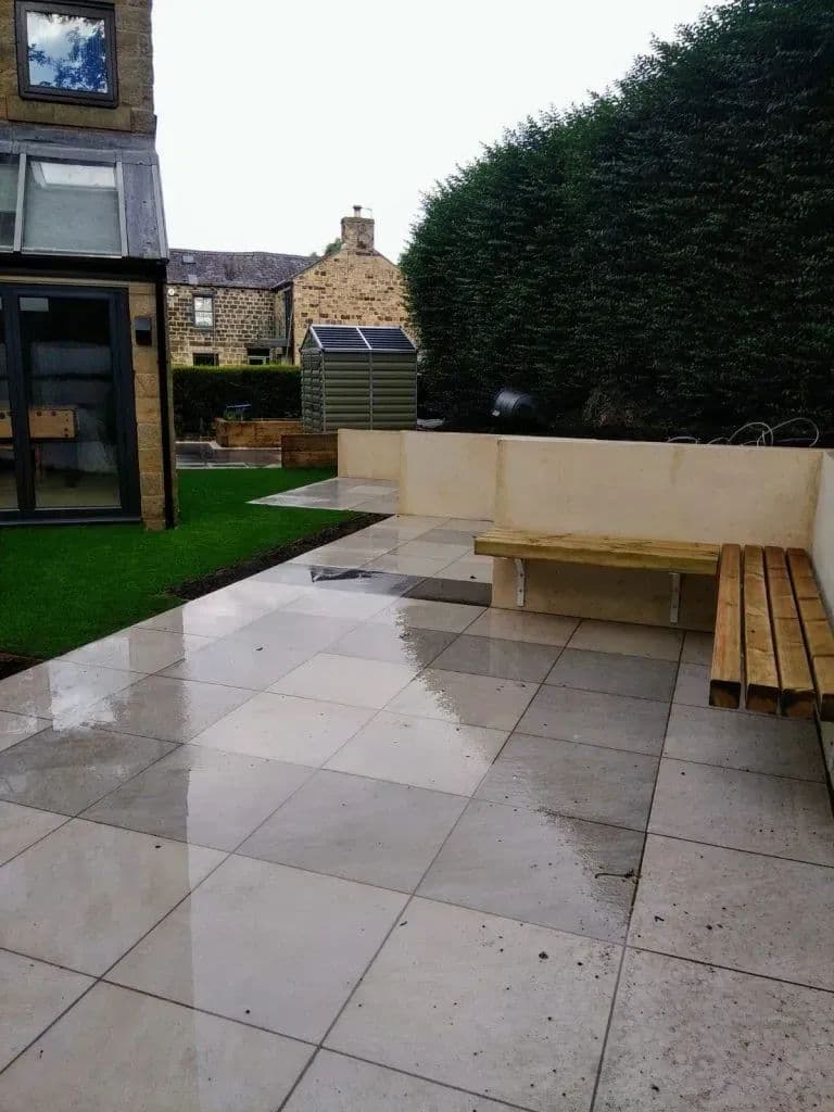 The finished patio with a bench and a strip of artificial lawn along the wall