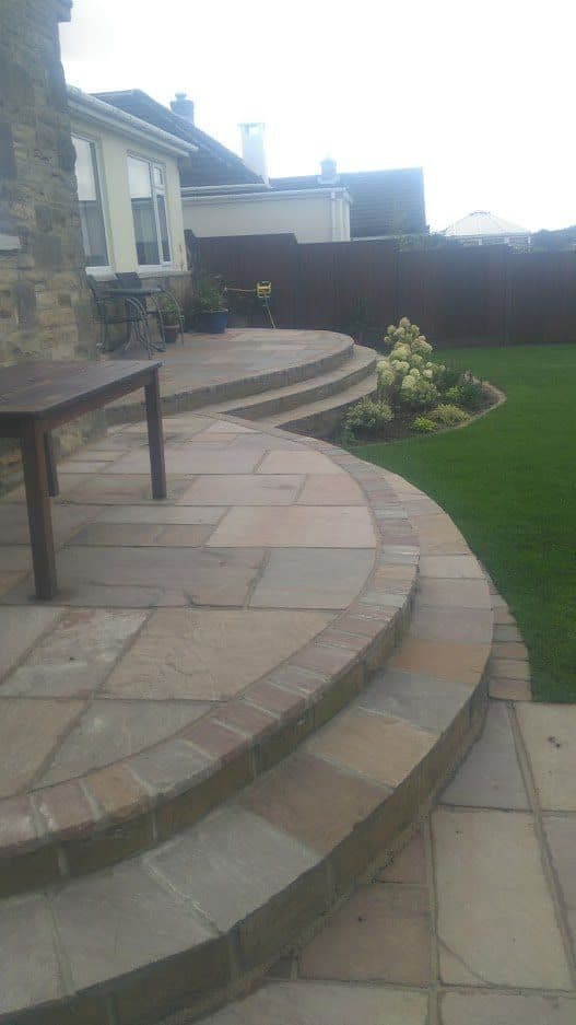 Wide curved sandstone steps sweeping down from a raised terrace to a lawn, with a planted border alongside