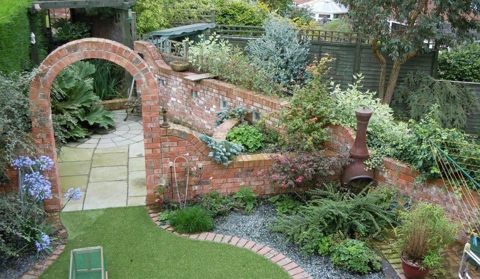 A designed back garden seen from above, with a brick wall built around a circular archway, sandstone paving, gravel and deep mixed borders