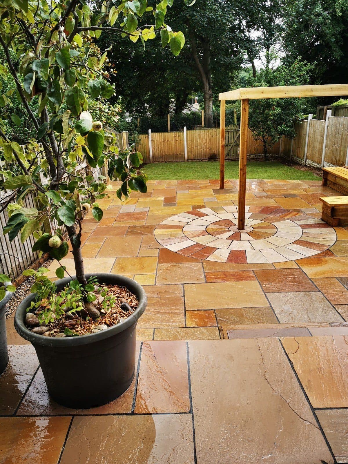 A riven sandstone patio with a paving circle at its centre and timber pergola posts standing in the slabs