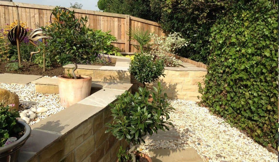 Sandstone-walled raised beds with flat coping stones, white gravel between them and shrubs newly planted