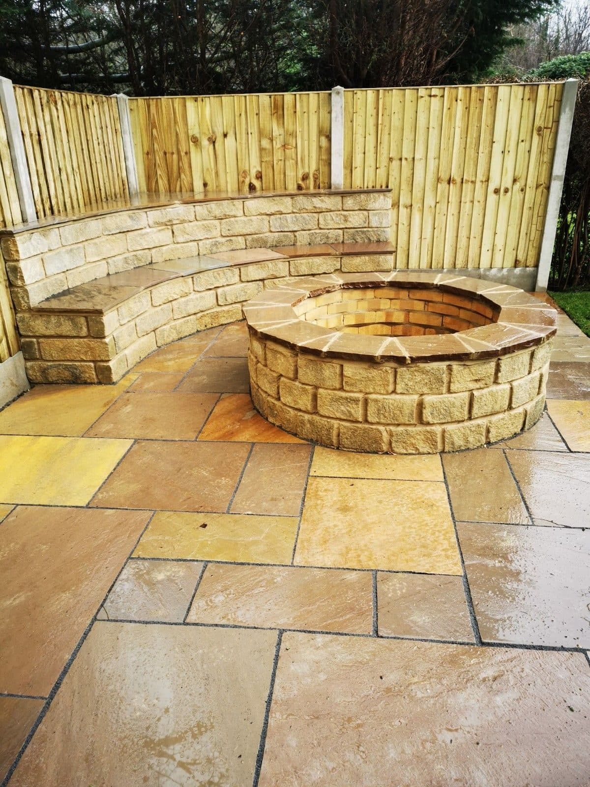 A curved sandstone seat wall around a circular stone fire pit on a riven sandstone patio