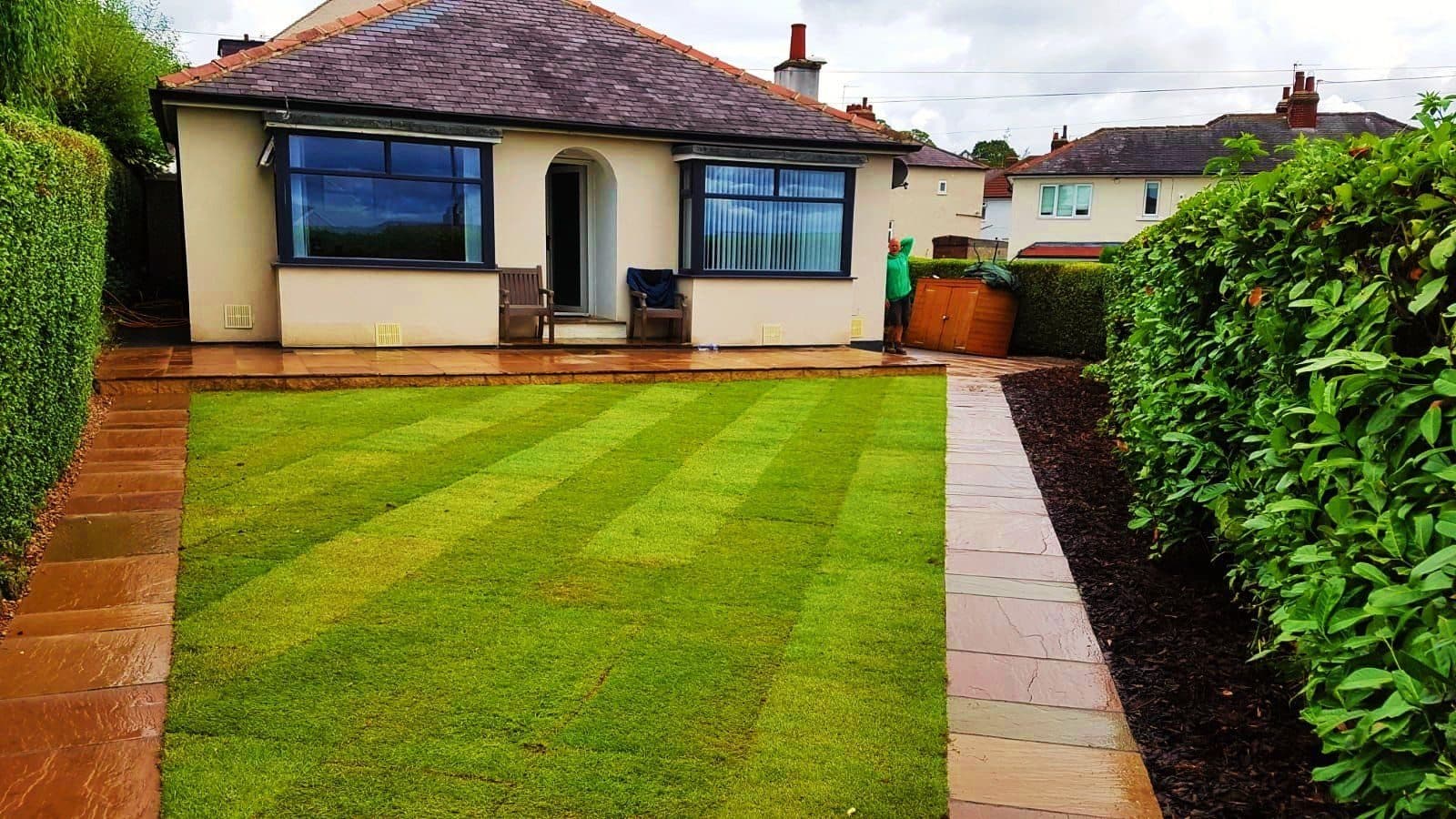 A rear garden with newly laid striped turf and a sandstone path running back to the house
