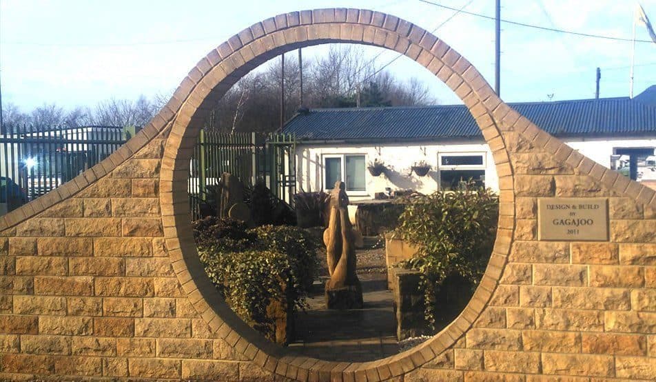 A stone garden wall built around a full circle, with a Gagajoo design-and-build plaque set into the stonework