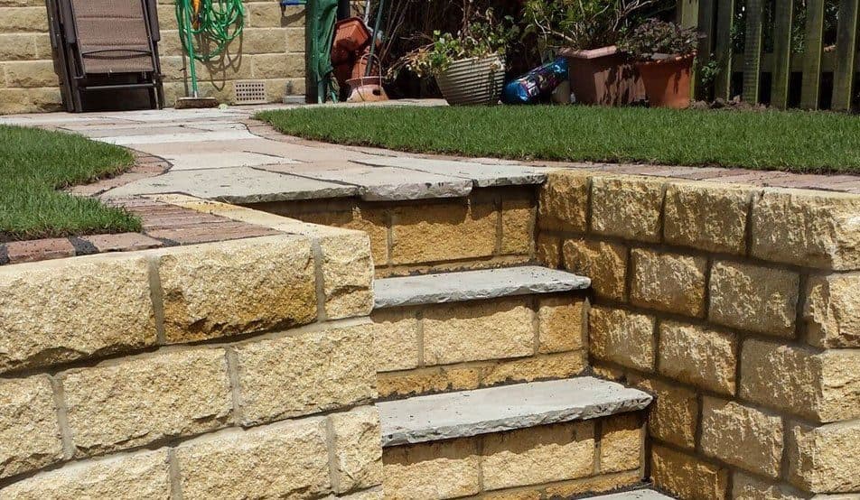 Stone steps set into a sandstone retaining wall, linking a lower lawn to an upper lawn and flagged path
