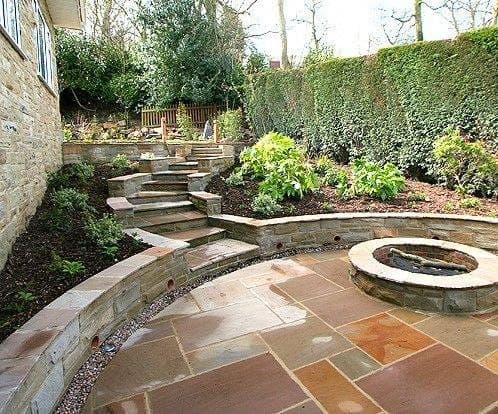 A terraced garden with curved sandstone retaining walls, steps to an upper level and a circular fire pit in the paving