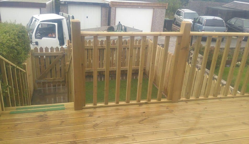 A raised timber deck with a spindle balustrade, and a matching picket fence and gate beyond it